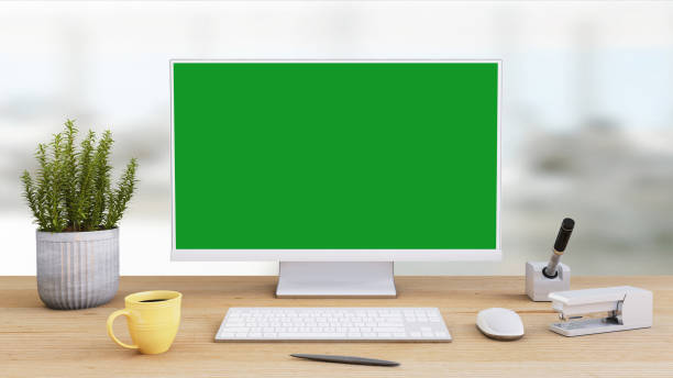 Office desk with large PC computer screen with green background - template Interior scene with large PC monitor computer screen of the office desk. Keyboard, mouse, coffee cup, table lamp. Green screen for easier copy space. Business template mock up for designers chroma key photos stock pictures, royalty-free photos & images
