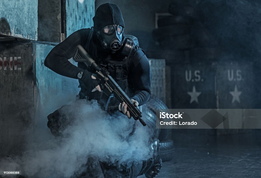 Gas mask wearing lone soldier in smoky indoor urban setting Special Forces Stock Photo