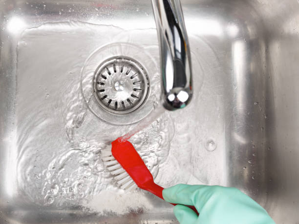 istock Hand with rubber glove holding red brush for scrubbing sink 913106664