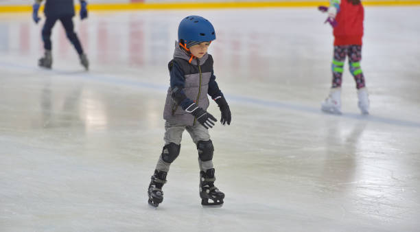 Adorable little boy in winter clothes with protections skating on ice rink stock photo