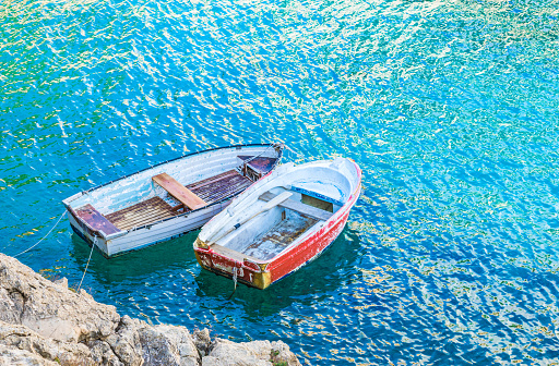 Two old rowboats moored at sea shore with turquoise colored water