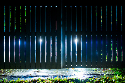 The car stands on the territory of the house at night. Light headlights through the fence