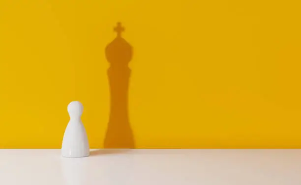 Chess pawn casting the shadow of a king over yellow background. Leadership and ego concept. Horizontal composition with copy space.