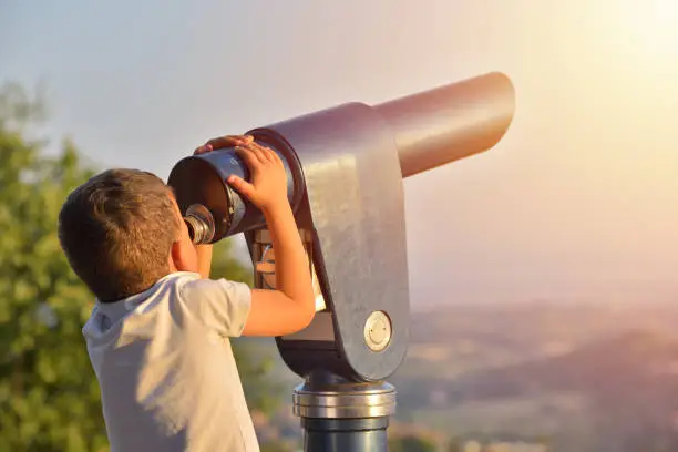 Photo of Little boy looking into tourist telescope eyepiece. Travel tourist destination landscape magnification