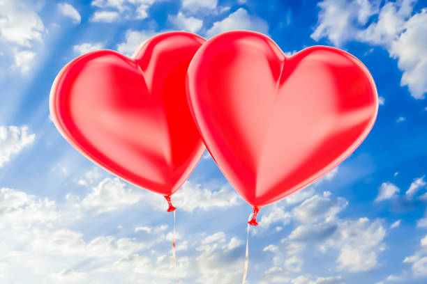 istock Two red balloons in the shape of hearts flying on a blue sky, 3D rendering 913178570