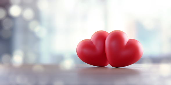 Red heart pair sitting over pale defocused background.  Panoramic composition with copy space.