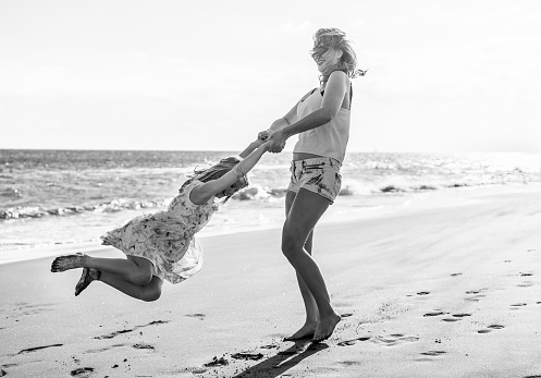 Mother and daughter having fun on tropical beach - Mum playing with her kid in holiday vacation next to the ocean - Family lifestyle and love concept - Black and white editing - Focus on baby girl