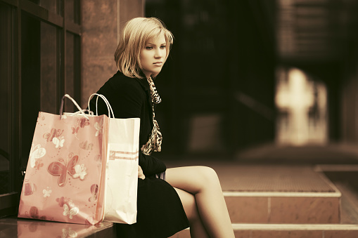 Sad young woman with shopping bags sitting on mall steps