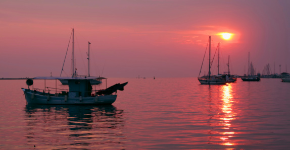 Sunset in a harbor, fishing boat on the left, yachts on the right