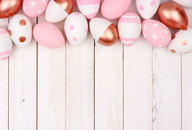 istock Easter egg top border. Rose gold, pink and white on white wood. 913200022