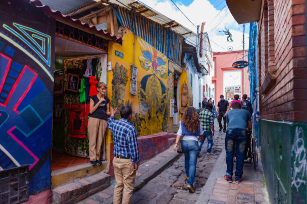 Bogotá, Colombia - Local Colombians On The Cobblestoned Calle del Embudo, In The Historic La Candelaria District of The Andean Capital City Bogota, Colombia - May 28, 2017: Local Colombian people walk up the narrow Calle del Embudo which gets its name from its shape. The English translation of the name would be, "Funnel Street." It is one of the most colorful streets in the historic La Candelaria district of Bogotá, the Andean capital city of the South American country of Colombia. Constructed over 450 years ago, the street leads to the Chorro de Quevedo, the plaza where it is believed the Spanish Conquistador, Gonzalo Jiménez de Quesada founded the city in 1538. Many street facing walls in this area are painted with either street art or the legends of the pre-Colombian era, in the vibrant colours of Colombia. Photo shot in the afternoon sunlight; horizontal format. Camera: Canon EOS 5D MII. Lens EF 24-70 mm F2.8L USM. calle del embudo stock pictures, royalty-free photos & images