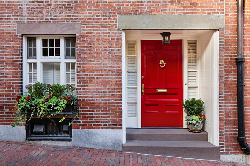 Color image depicting the exterior of a building on a traditional city street in London, UK. The house has a pretty red door which is surrounded by lush foliage.