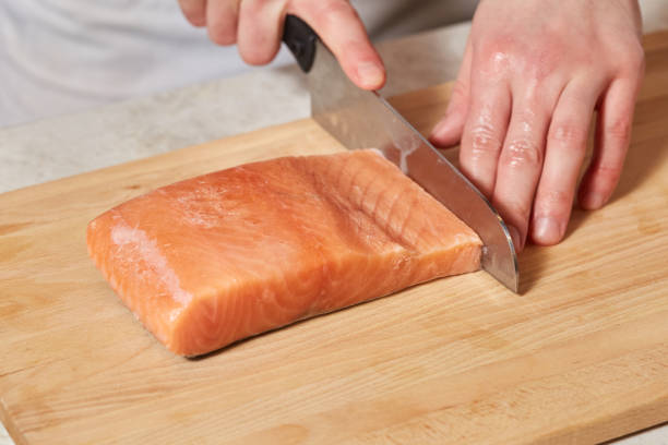 istock Chef making sushi rolls. Cutting salmon fish on wooden board 913252338