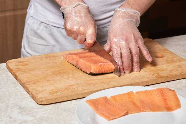 istock Chef making sushi rolls. Cutting salmon fish on wooden board 913252344