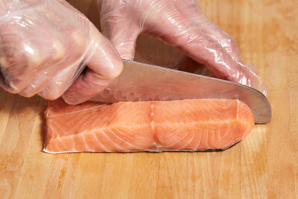 istock Chef making sushi rolls. Cutting salmon fish on wooden board 913252346