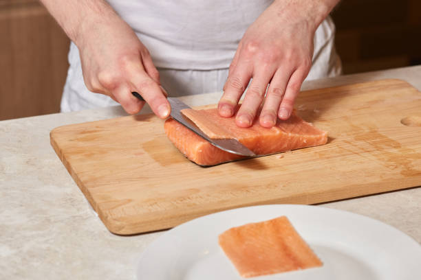 istock Chef making sushi rolls. Cutting salmon fish on wooden board 913252350
