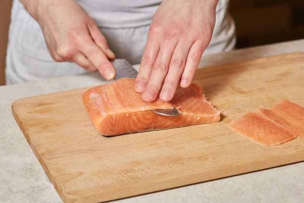 istock Chef making sushi rolls. Cutting salmon fish on wooden board 913252434
