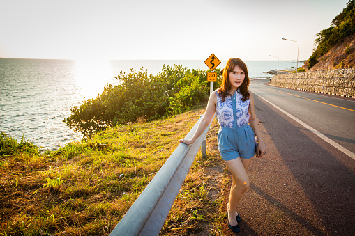 An Asian woman, age 30s, in casual dress on the sea-side road