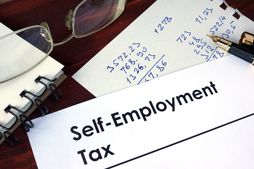 Paper with words self-employment tax on a wooden background.