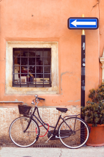 A bike and basket resting on a bstucco building with a directional arrow above the bike.