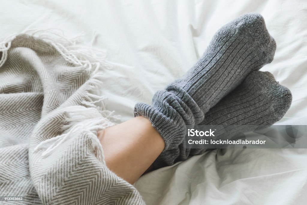 Feet crossed with gray socks on bed under blanket Pair of feet in gray socks on a bed under a cozy blanket. Sock Stock Photo