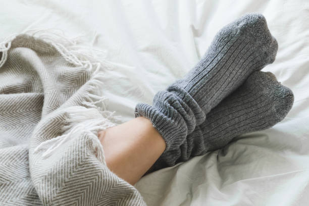 Feet crossed with gray socks on bed under blanket Pair of feet in gray socks on a bed under a cozy blanket. sock photos stock pictures, royalty-free photos & images