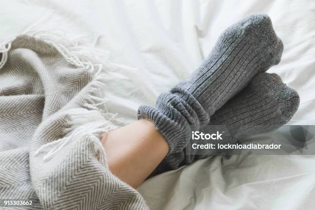 Feet Crossed With Gray Socks On Bed Under Blanket Stock Photo - Download Image Now - Sock, Cold Temperature, Bed - Furniture