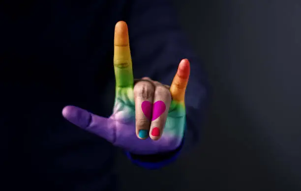 Love for Gay and Homosexual Concept, Midsection Of Man With Colorful Hand Guesture in means "I Love You" with Heart and Rainbow Color Against Dark Background