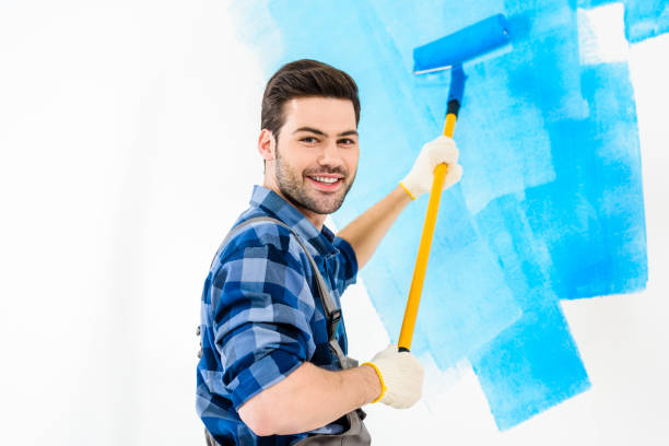 istock smiling handsome man painting wall with blue paint 913311384