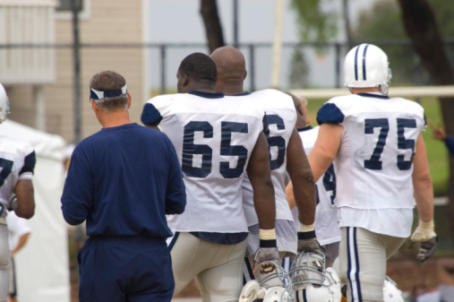 Three American Football players in full tackle football pads stand as a team ready to play. Image taken in Utah, USA.