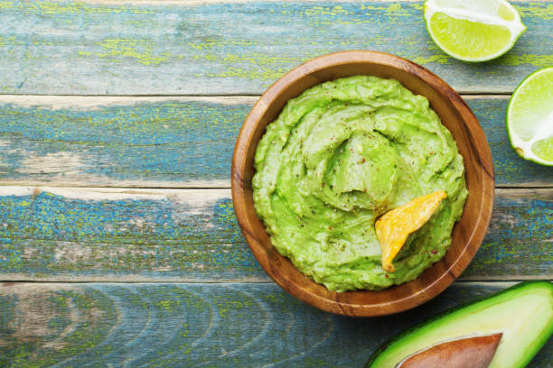 Green guacamole with  ingredients avocado, lime and nachos on wooden vintage table top view. Green guacamole with  ingredients avocado, lime and nachos on wooden vintage table top view. Traditional mexican food. guacamole stock pictures, royalty-free photos & images