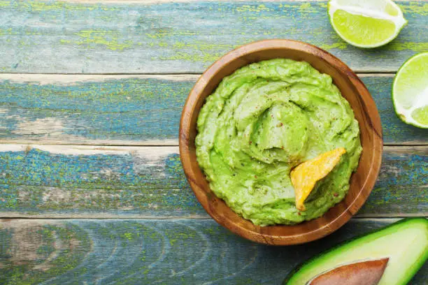 Photo of Green guacamole with  ingredients avocado, lime and nachos on wooden vintage table top view.