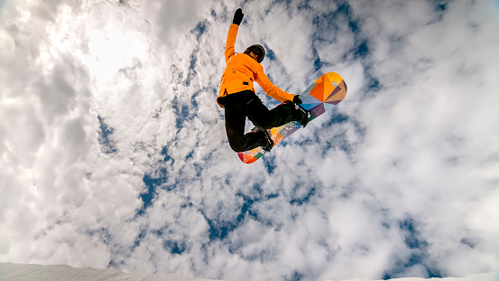 Woman jumping in air with snow board on half pipe against fluffy clouds.