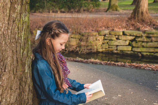 istock Young Girl Reading Against Tree 913325902