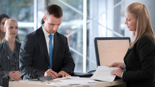 istock Female bank teller helping male customer with documents he needs to sign 913326898