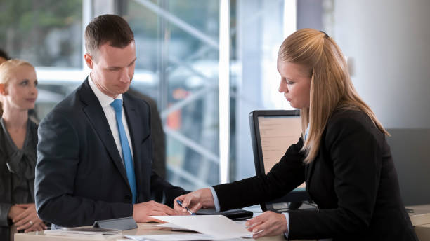 istock Female bank teller helping male customer with documents he needs to sign 913326904