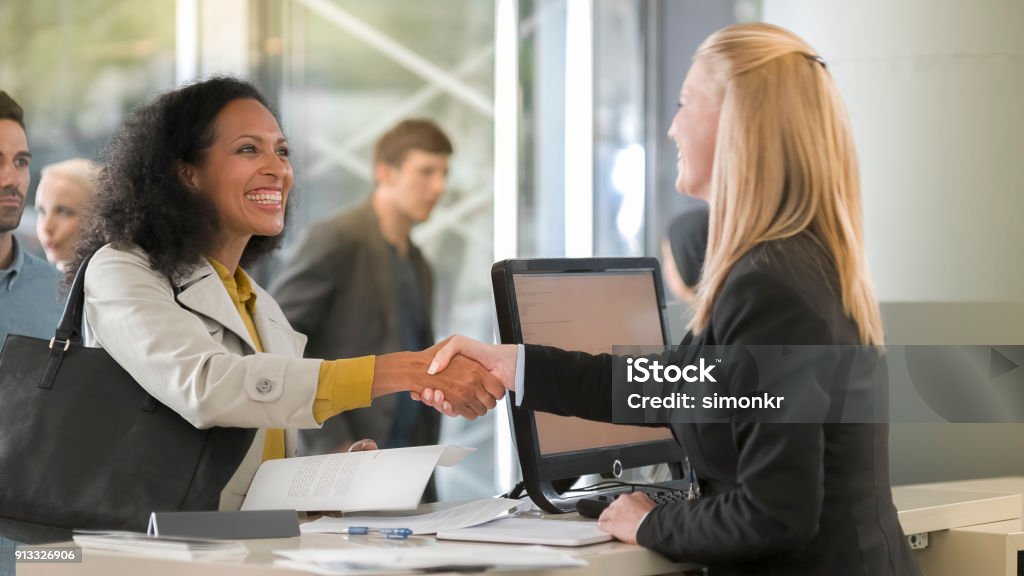 Female rental clerk giving documents to female customer renting car Female rental clerk giving her female customer copy of contract to rental car. Bank Teller Stock Photo