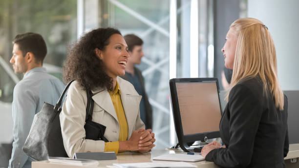 Woman asking rental agent for rental car type and female agent helping her Woman at counter in car rental office asks agent for rental car. bank teller stock pictures, royalty-free photos & images