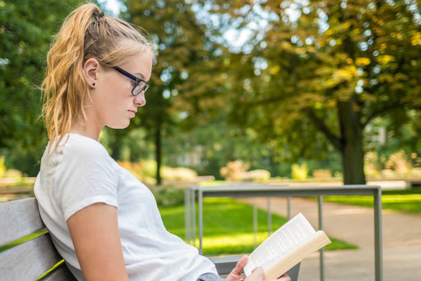 istock A schoolgirl is sitting on a park bench reading a book 913331076