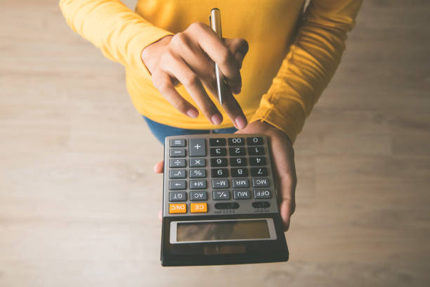 woman using a calculator with a pen in her hand - calculator imagens e fotografias de stock