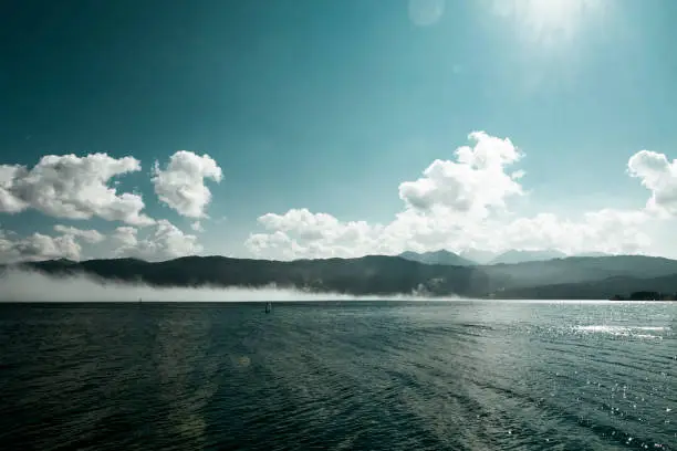 View in good weather over a lake, to mountains shrouded in fog