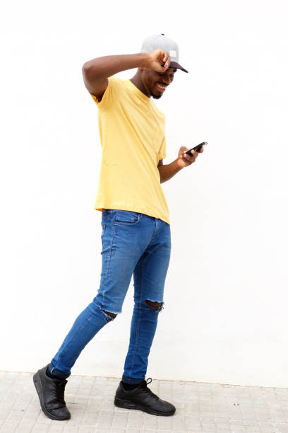 Full length cool young black with cellphone against white wall