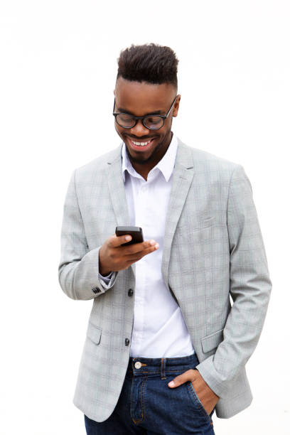jeune homme d’affaires souriante regardant téléphone mobile - isolated on black young adult portrait business photos et images de collection