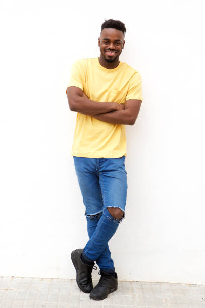 istock Full length smiling young black man leaning against white wall 913338276