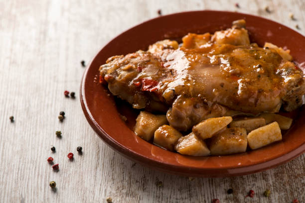 closeup of a brown earthenware plate with manitas de cerdo, spanish stewed pigs trotters, on a white rustic wooden table