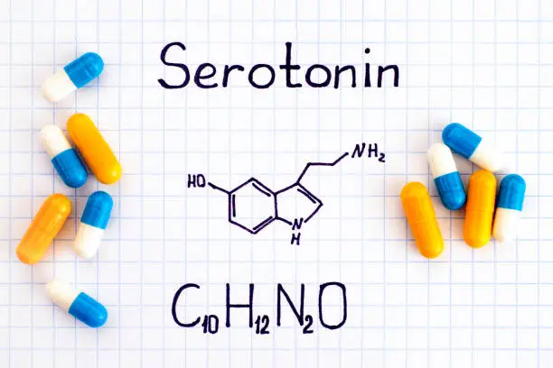 Chemical formula of Serotonin with some pills. Close-up.