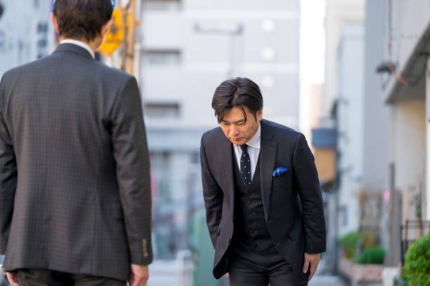 uomo d'affari giapponese maturo che si inchina per mostrare rispetto - bowing foto e immagini stock