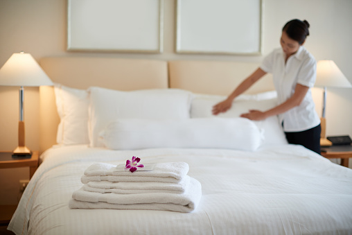 Hotel room service. Young woman maid making bed at the hotel room