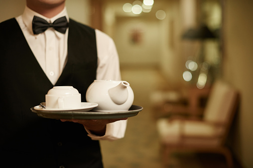 Cropped image of waiter holding tray with teapot and cup