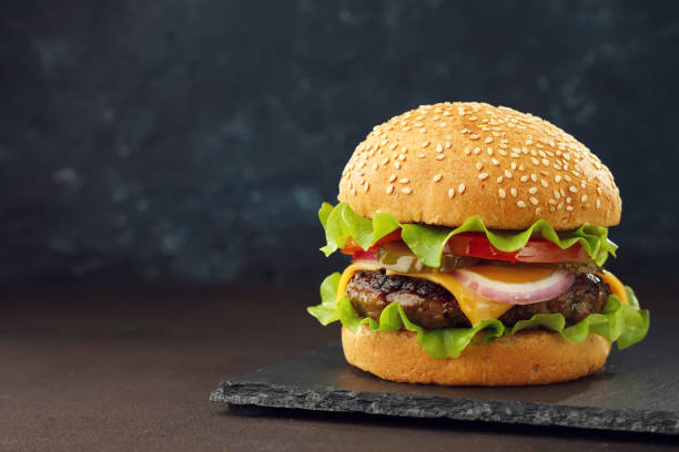istock Homemade burger with beef cutlet, cheddar, lettuce and vegetables on slate board. 913387138